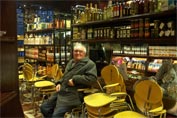 Jim resting on stacking chairs in Peckham's deli backed by shleves