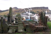View of the site framed by gravestones on the side of Calton HIll, with Salisbury Crags in the background